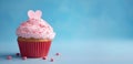 festive cupcake with pink icing, decorated with pink heart with small sprinkles, on blue background