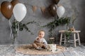 Festive decor for one year toddler, boy sitting on the floor with cake, gray background with brown and white balloons
