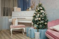 Festive decorated fir-tree in living room with piano, pink sofa and wrapped Christmas gifts. Tender color palette in interior Royalty Free Stock Photo
