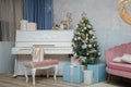 Festive decorated fir-tree in living room with piano, pink sofa and wrapped Christmas gifts. Tender color palette in interior Royalty Free Stock Photo