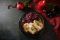 Festive dinner, roast pork slices with red cabbage on a dark plate, red candles, wine and Christmas decoration on a dark