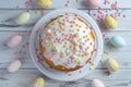 Festive Easter cake with colorful candy toppings and pastel eggs on wooden background.