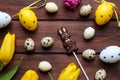 Festive flat lay with yellow tulips, chocolate Easter bunny, and decorative eggs on a rustic wooden table. aster background. Top