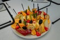 Festive fruits plate with cut fruit pieces on skewers in white plate. Dessert for birthday party, sweet appetizer. Banana, apple,