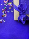 Festive gift wrapped present box with blue satin bow, decorated with colorful stars, close up isolated on trendy blue background Royalty Free Stock Photo