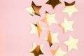 Festive gold glossy stars on pastel pink background, top view, border.