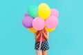 Festive image of unknown woman covering her head and holding in hands bunch of balloons on blue wall