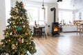 Festive interior of house is decorated for Christmas and New Year in loft style with black stove, fireplace, Christmas tree. Warm Royalty Free Stock Photo