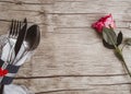 Light pastel colored tableware set: vintage silverware on napkin and delicate pink rose on rustic shabby wooden background with