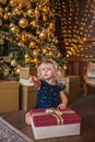 Festive little blonde girl opening a gift at home in the living room with Christmas decoration and showing somewhere with her