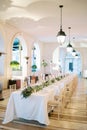 Festive long table with bouquets of flowers in a large hall with glowing chain lamps on the ceiling