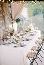 Festive long table on the terrace of an old house under a cover with glowing light bulb garlands