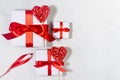 Festive love background - white gift boxes with red silk ribbons, sweet lollipops hearts on white wood board, top view. Royalty Free Stock Photo