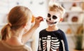 Festive makeup for Halloween. Woman doing skeleton make-up for boy in costume while preparing holiday