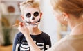 Festive makeup for Halloween. Woman doing skeleton make-up for boy in costume while preparing holiday