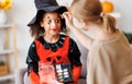 Festive makeup for Halloween. Woman doing witch make-up for ethnic curly girl in costume while preparing holiday