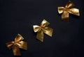 Festive minimalistic background with three glossy golden gift bows. Black backdrop. Top view