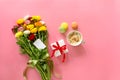 Festive morning concept buttercup flowers bouquet, gift box, cup of cappuccino and makarons cake on the pink background with copy