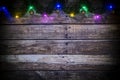 Festive New Year or Christmas background of dark old wooden boards, glowing garland of colored lights and Christmas balls Royalty Free Stock Photo