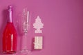 Festive New Year concept. A bottle of pink champagne and a glass for it on a pink background. Christmas tree, garland and gift box Royalty Free Stock Photo