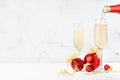 Festive New Year drink - sparkling flow of champagne pouring from neck bottle in two glasses and shiny red decoration - balls. Royalty Free Stock Photo