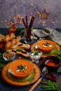 Festive New Year`s table setting. Tomato soup in bright orange plates against a background of garlands and stars Royalty Free Stock Photo