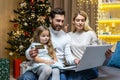 A young family sitting at home, holding a laptop and a credit card, choosing Christmas gifts online Royalty Free Stock Photo