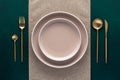 Festive place setting with beige napkin. Empty plates and gold cutlery on dark green background. Top view. Dining table in luxury Royalty Free Stock Photo