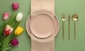 Festive place setting with beige napkin and spring flowers. Empty plates and gold cutlery on green background. Top view. Dining Royalty Free Stock Photo