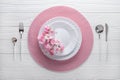 Festive place setting with pink napkin and spring flowers. Empty plates and silver cutlery on white wooden table. Top view. Royalty Free Stock Photo