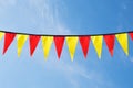 Festive ribbon of red and yellow triangle flags on the white clouds and blue sky background Royalty Free Stock Photo