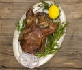 Festive roast duck on a platter with dill on a wooden table.