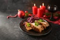 Festive roast pork slices with red cabbage on a dark plate, red candles, wine and Christmas decoration against a dark background, Royalty Free Stock Photo