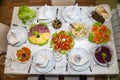 Festive set table with plates of salads, appetizer of vegetables and fruits, sliced sausage cheese, top view. Holiday, food