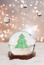 A festive snow globe featuring a green Christmas tree, surrounded by sparkling lights and a snowy base. 3d rendering
