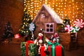 Festive snowman on background of blurred Christmas interior with wooden house, candy, tree and gifts. No people. Holiday Royalty Free Stock Photo