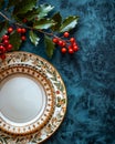 Festive Table Setting with Elegant Porcelain Dinnerware and Red Holly Berries on a Dark Blue Textured Background