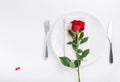 Festive table setting. Empty plate, knife, fork, napkin and red rose on white table. Top view, flat lay, copy space Royalty Free Stock Photo