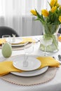 Festive table setting with glasses, burning candle and vase of tulips. Easter celebration Royalty Free Stock Photo