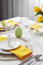 Festive table setting with glasses, burning candle and vase of tulips. Easter celebration Royalty Free Stock Photo