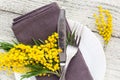 Festive table setting plate with napkin fork and knife and mimosa flower decoration on white wooden background Royalty Free Stock Photo