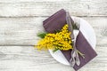 Festive table setting plate with napkin fork and knife and mimosa flower decoration on white wooden background Royalty Free Stock Photo