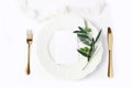 Festive table summer setting with golden cutlery, olive branch, porcelain dinner plate and silk ribbon on white table