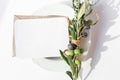Festive table summer setting with olive leaves branch on porcelain plate. Blank paper card mockup scene with shadow.