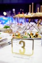 On the festive table with a white tablecloth are two crystal empty glasses for drinks  and a metal plate with number three, Royalty Free Stock Photo