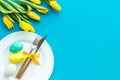 Festive traditional Easter dinner concept. Tableware, painted eggs, tulips flowers on blue table top view copy space Royalty Free Stock Photo