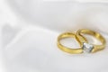 Festive wedding background with two gold rings with diamond on white satin material. Copy space. Royalty Free Stock Photo