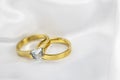 Festive wedding background with two gold rings with diamond on white satin material. Copy space. Royalty Free Stock Photo