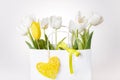 Festive white, yellow tulips composition, handmade heart, ribbon on white background. Bouquet of spring flowers in white paper bag