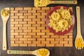 Fettuccine and Farfalle pasta on a red plate on a bamboo substrate and wooden spatulas on a mahogany background